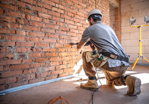 Handyman at a construction site in the process of drilling a wall with a perforator.
